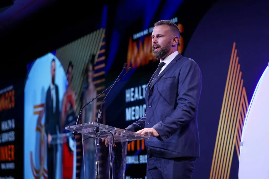 Dr Adam Sheriff, chiropractor at Noosa Junction Chiropractic, speaking at the podium after winning the 2025 Sunshine Coast Business Award for Health & Medical Services